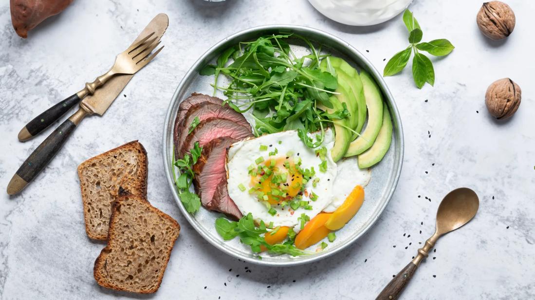 Plate with beef, eggs, avocado, leafy greens and apricots, with multi-grain bread, walnuts, sweet potato and yogurt