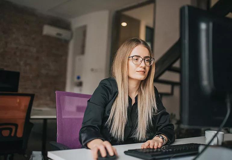 A person with long hair working on a computer while wearing blue light glasses