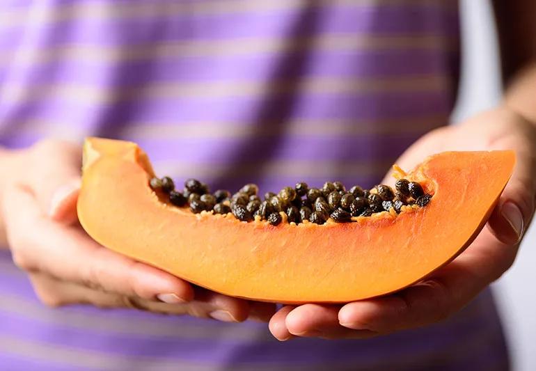 A close up of a person holding a slice of papaya fruit with the seeds
