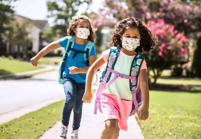 covid masked children with backpacks running home from school