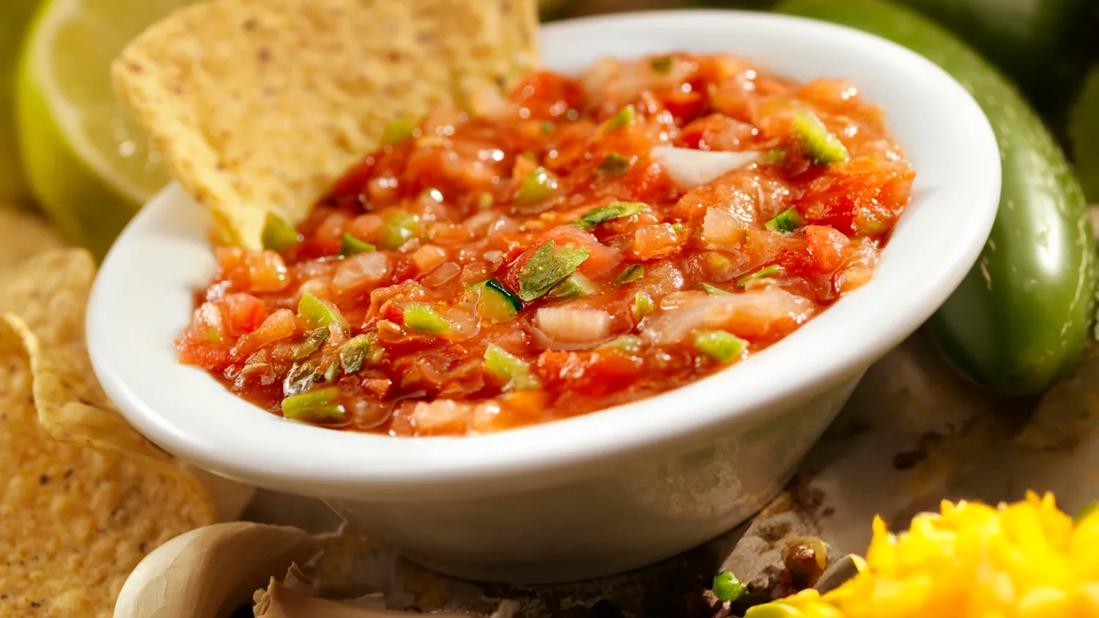 Small bowl of salsa, with chips, peppers, lime and garlic around bowl