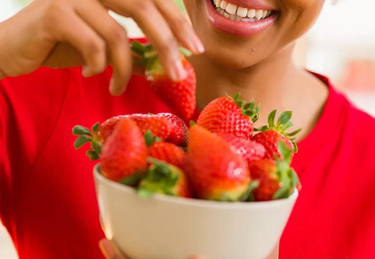 Person eating fresh strawberries from a white bowl.