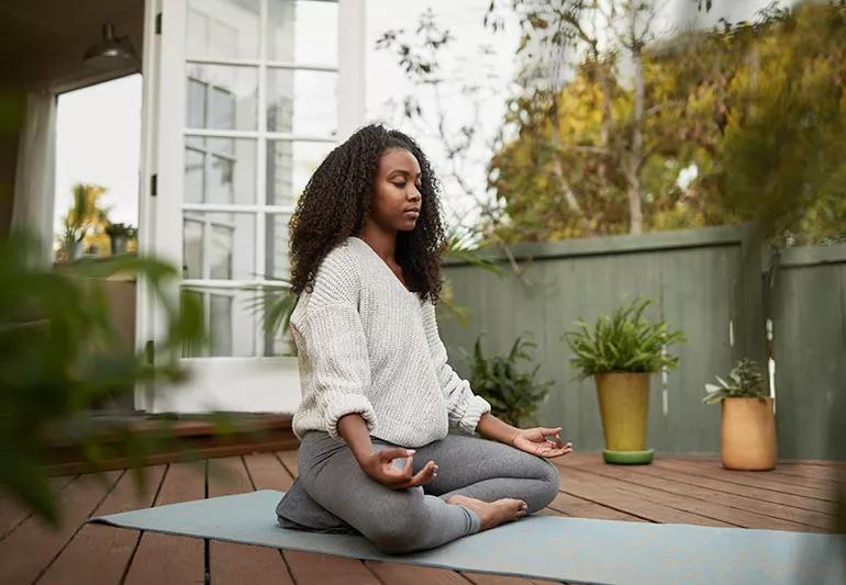 Person meditating on an outdoor deck surrounded by plants
