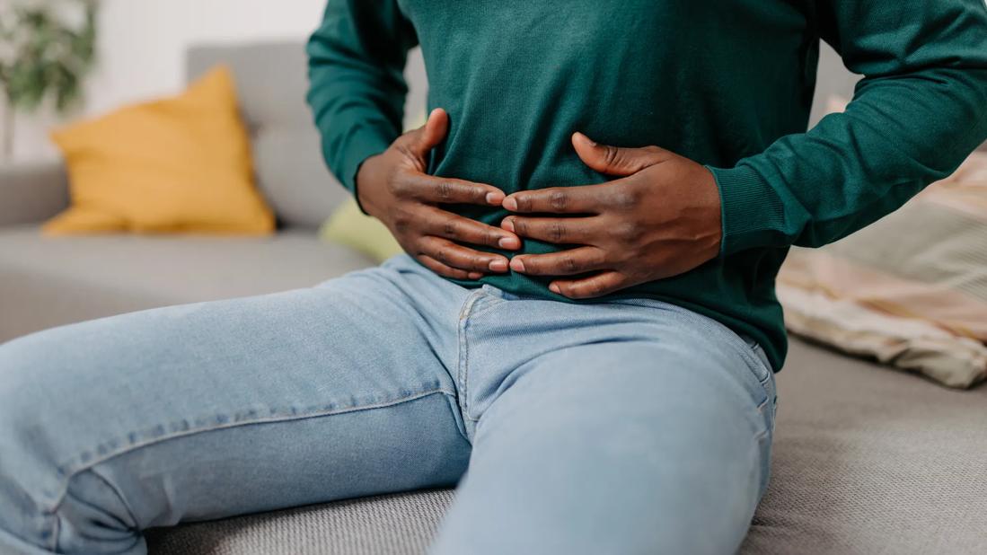 Person sitting down, holding abdomen with both hands