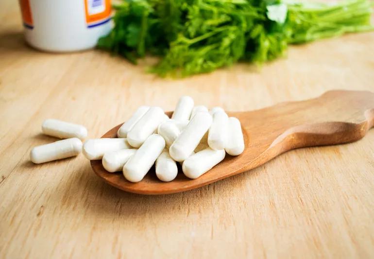 Vitamin K supplements in foreground with leafy veggies rich in vitamin K in background