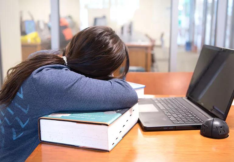 Person sleeping on dictionary, too tired to study.