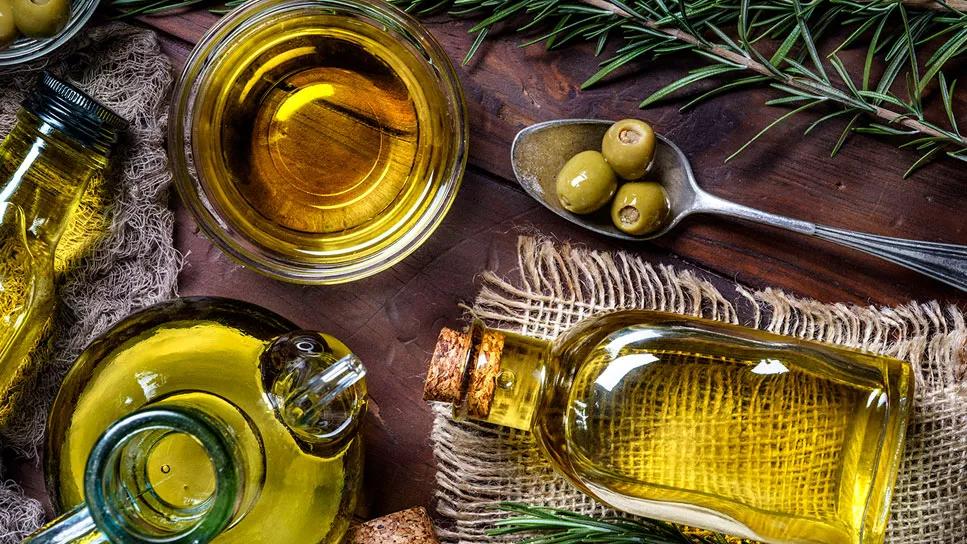 assorted vessels of olive oil on a wooden table with olives in spoon