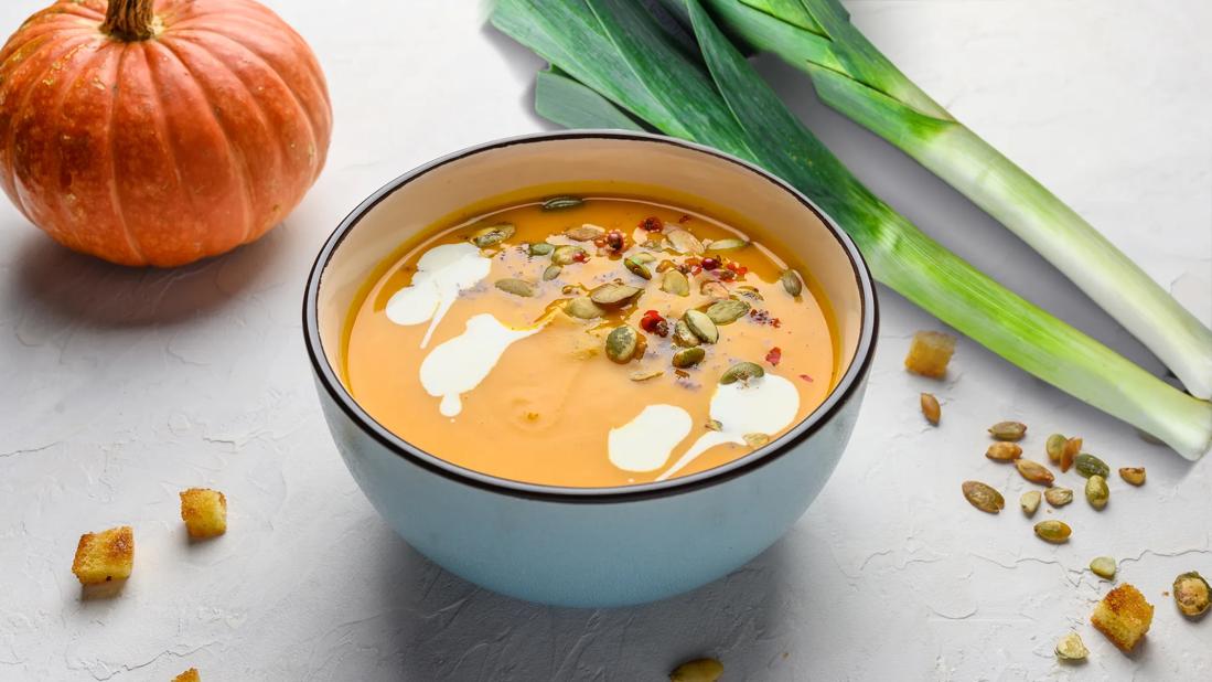 Bowl of pumpkin leek soup, with pumpkin and leek stalk on table