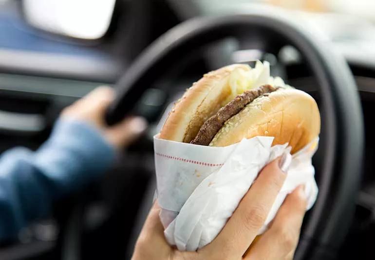 Woman driving and eating a hamburger