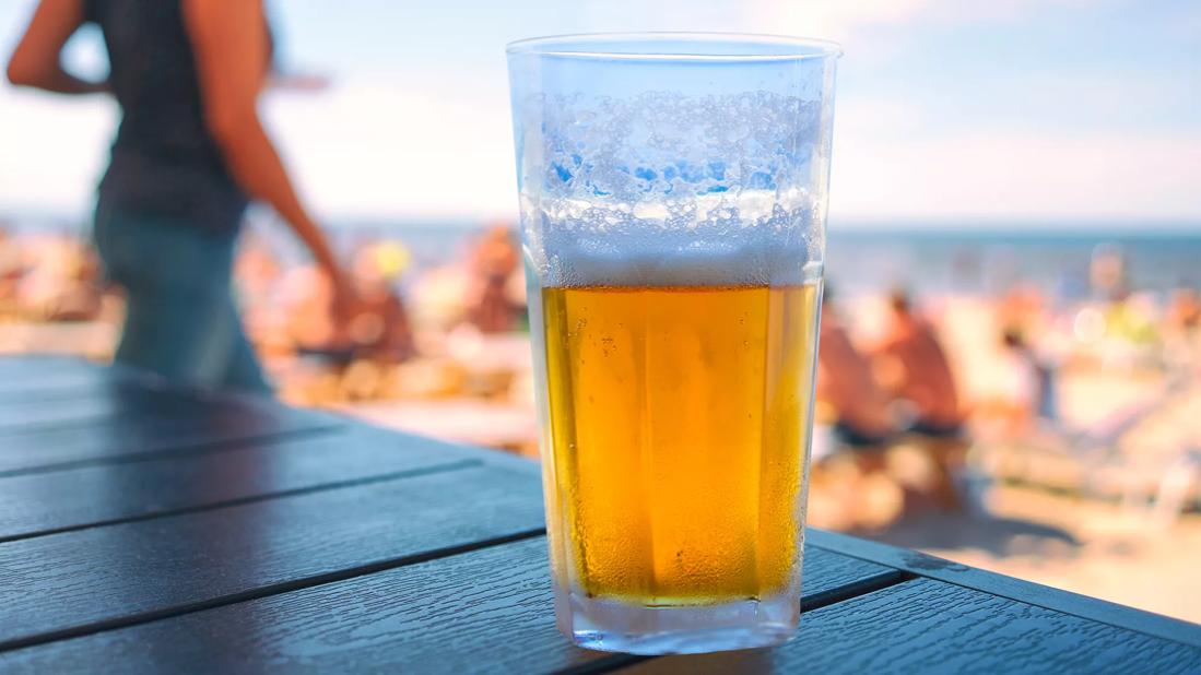 Glass of beer on table at beach with beach-goers