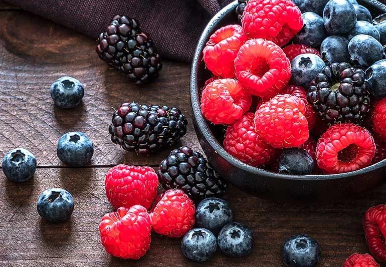 Raspberries, blackberries and blueberries in a black bowl on a wooden table