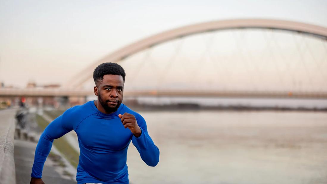 Man running intently on path outside, arched bridge nearby