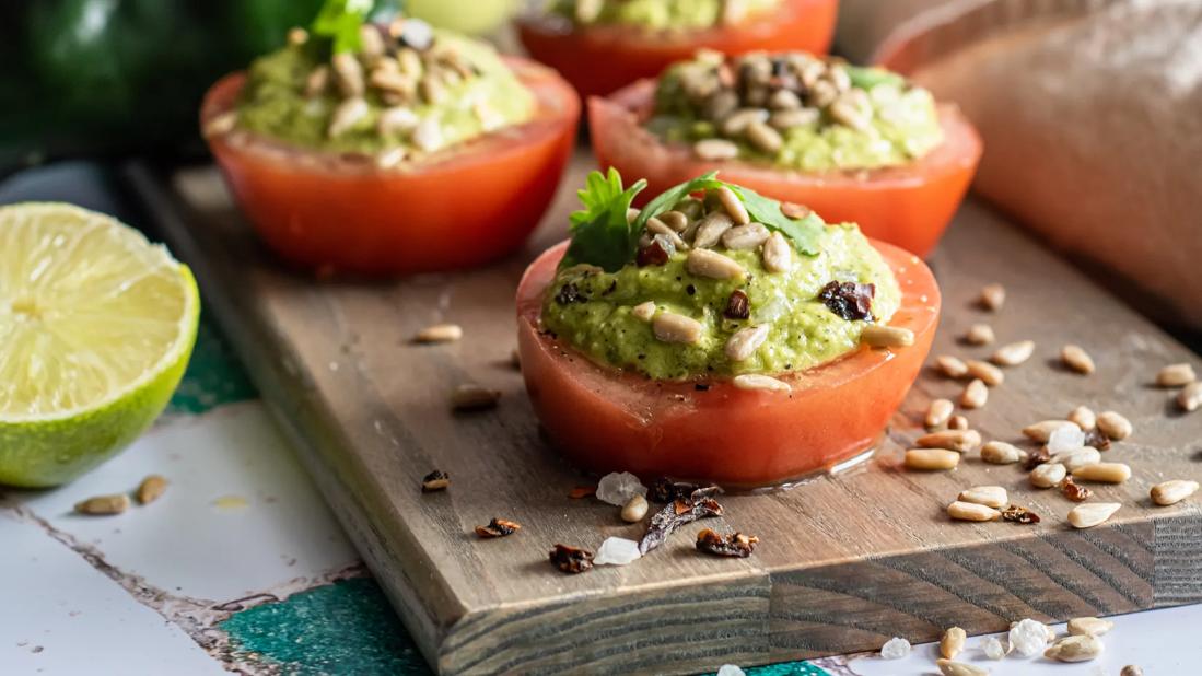 Tomatoes stuffed with poblano peppers and avocado on cutting board, with line and pumpkin seeds scattered