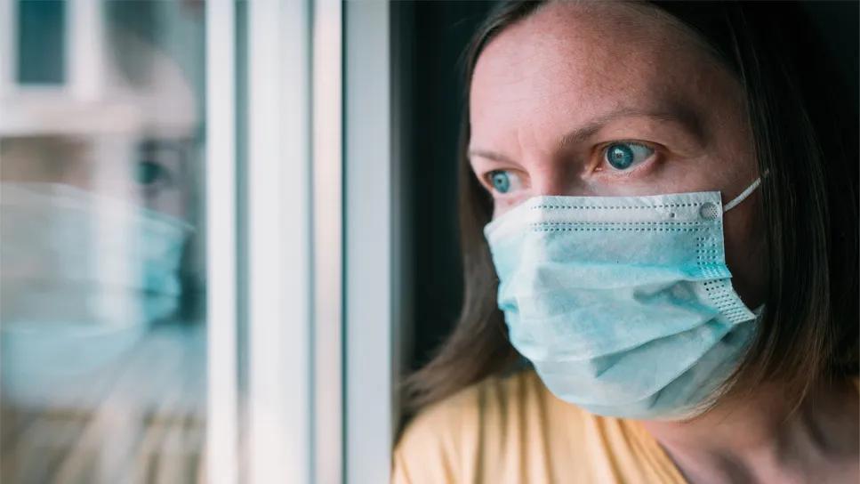 middle-aged woman with surgical mask looking out a window