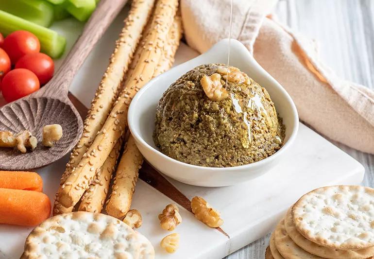 Scoop of mushroom walnut pate in a white bowl surrounded by crackers and vegetables