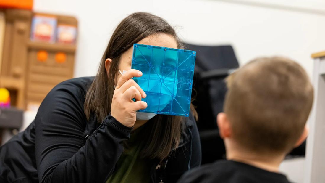 Caregiver holds object in front of face while engaging with child