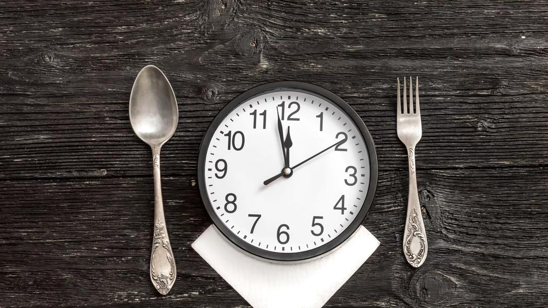 A fork and spoon alongside a clock with the time approaching 12 o'clock.