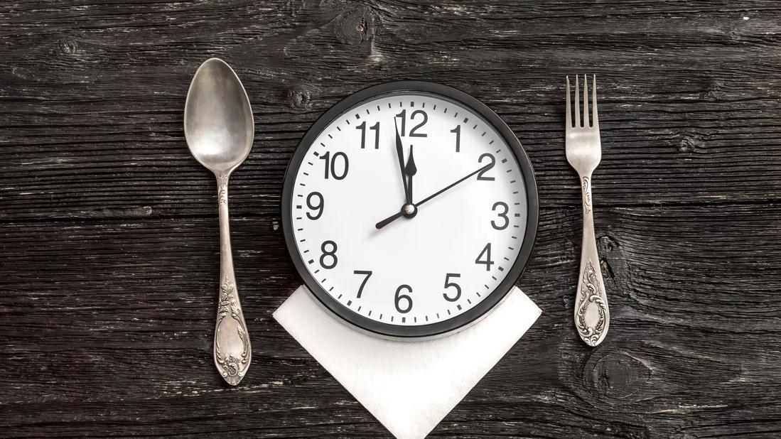 A fork and spoon alongside a clock with the time approaching 12 o'clock.