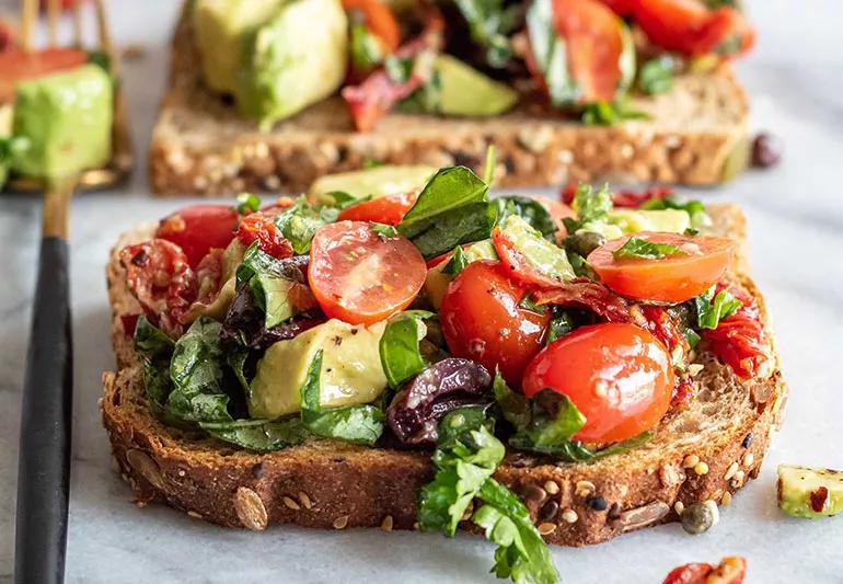 A piece of whole wheat bread covered by bruschetta with avocado, cherry tomatoes and lettuce