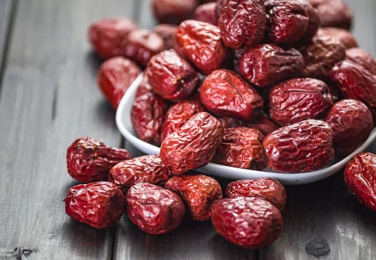 Dried Jujube fruit overflowing a white bowl on a wooden table.