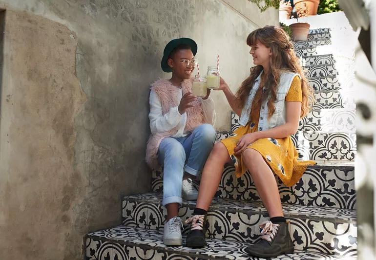 Two teen age girls drink lemonade on stairs