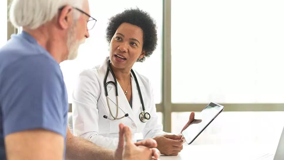 older male patient speaking with doctor holding tablet in office