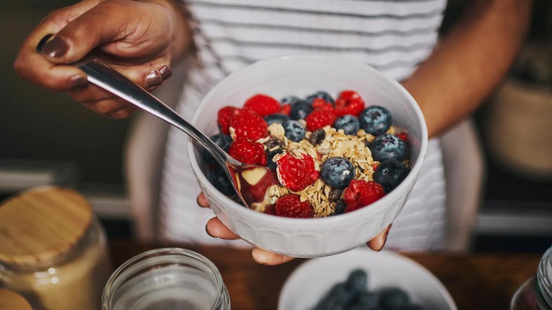 Person holding white bowl of healthy berries and oats, with spoon