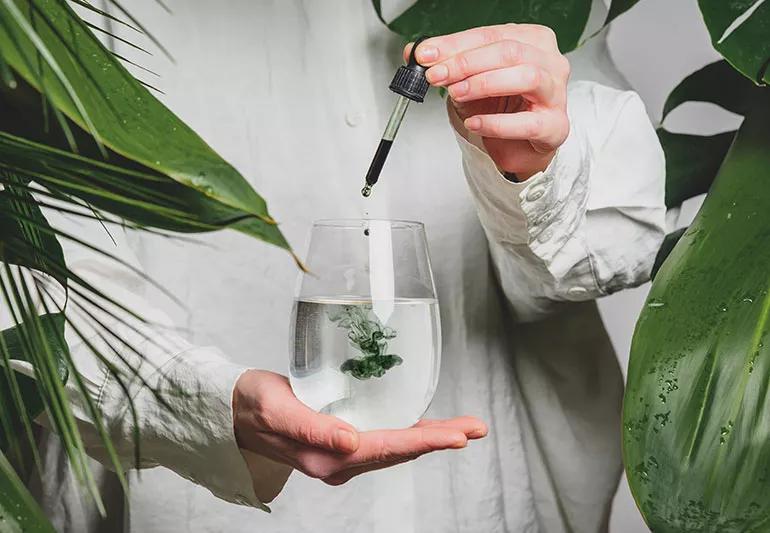 A person using an eyedropper to squeeze out dark-green chlorophyll drops into a clear liquid