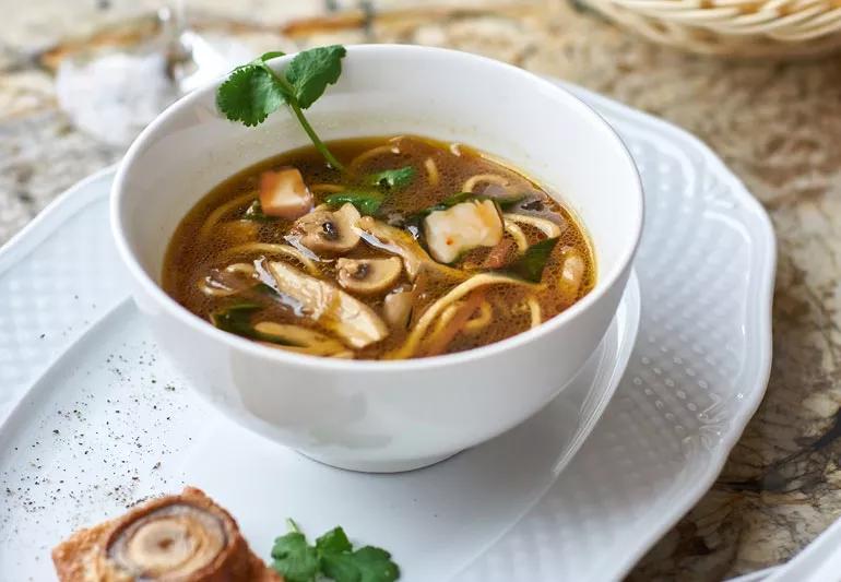 A white bowl of soba tofu and spinach noodle soup garnished with cilantro