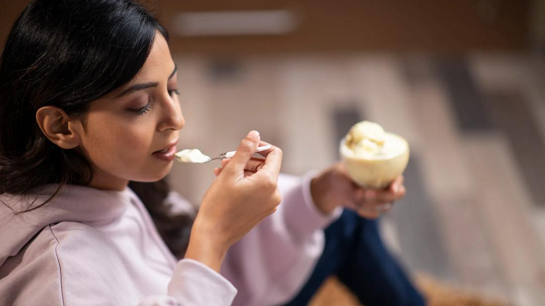 Person eating a spoonful of ice cream, holding a glass bowl of ice cream