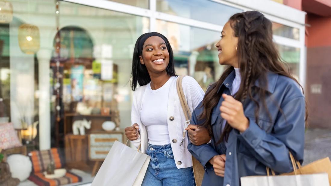 Two smiling people walking with shopping bags outside of stores