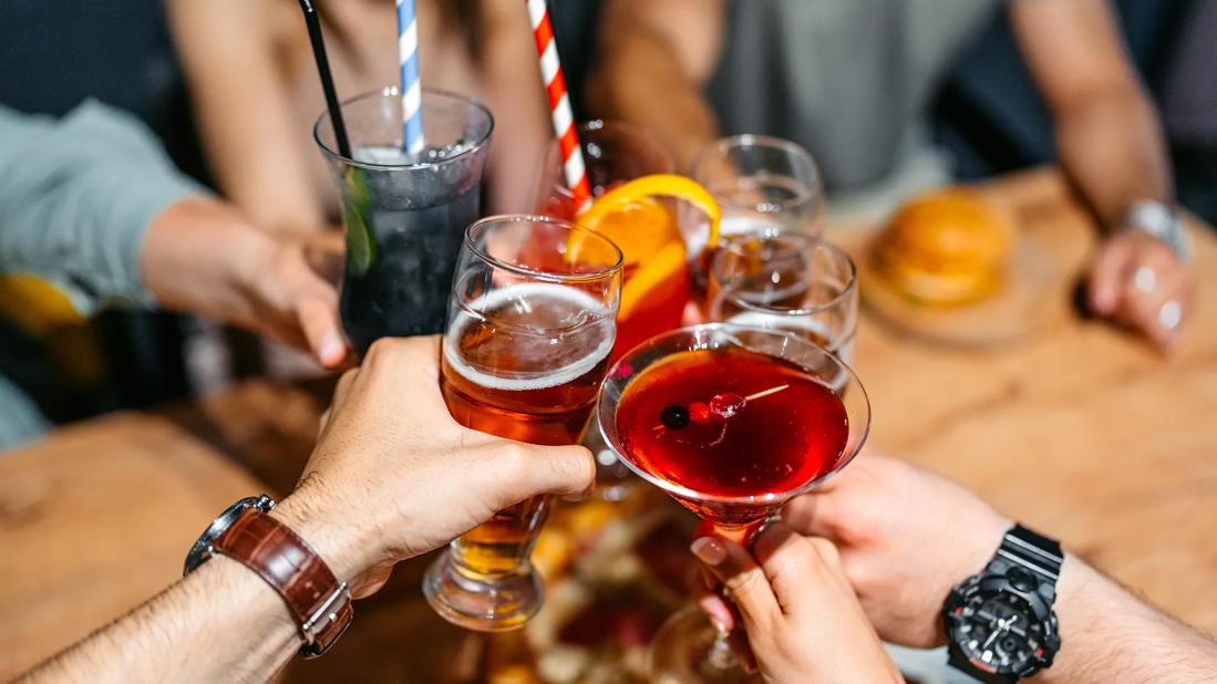 Multiple hands and a variety of glasses and drinks raised together in a toast