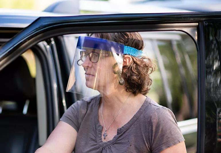 Woman getting out of her car wearing a face shield to protect from coronavirus