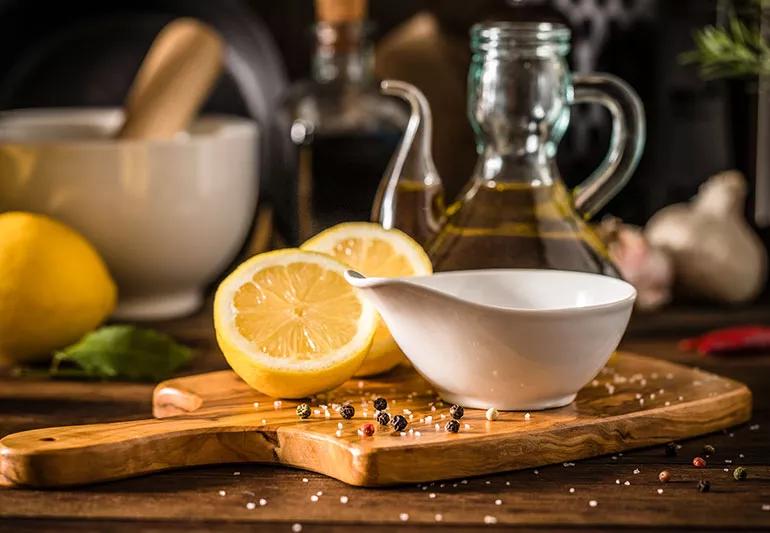 White serving bowl on a wooden cutting board surrounded by pepper, lemsurroundedons and olive oil