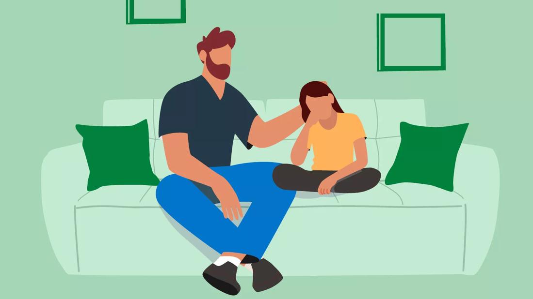 Man seated on a couch with his hand on the back of am small child as if comforting her