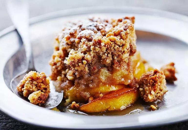 A portion of apple crisp with crumble top and baked apples on a white plate.