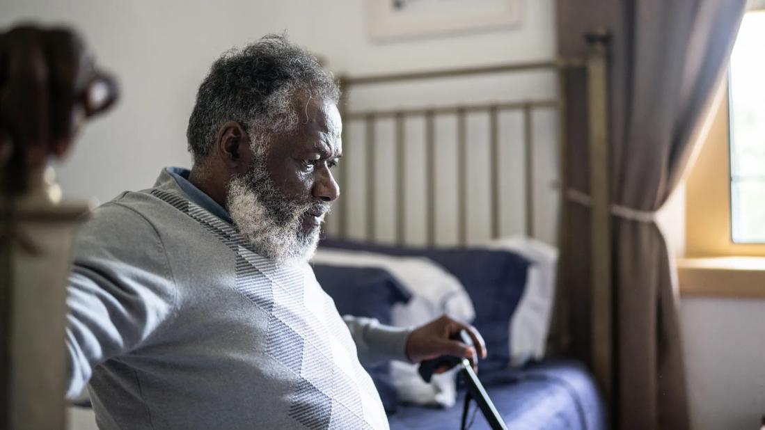 Older person with cane, sitting down on bed