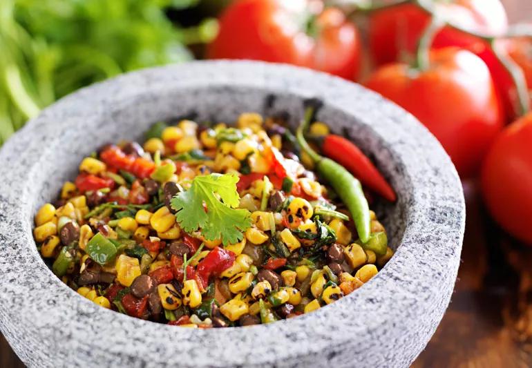 A bowl of salsa made of charred yellow corn, pinto beans, onions and tomatoes