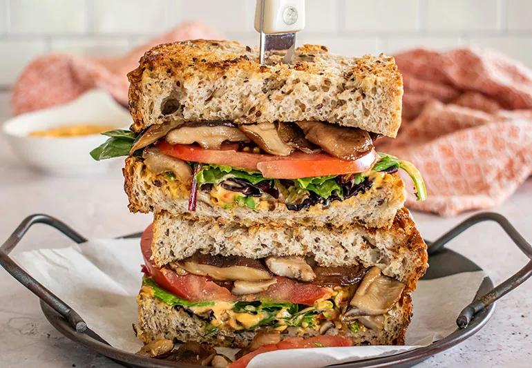 two halves of a shiitake mushroom sandwich piled atop one another with a knife sticking through them