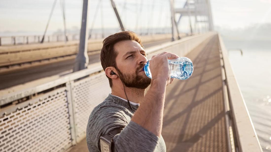 Person stopped on bridge during workout, wearing arm band and earbuds, to drink from water bottle