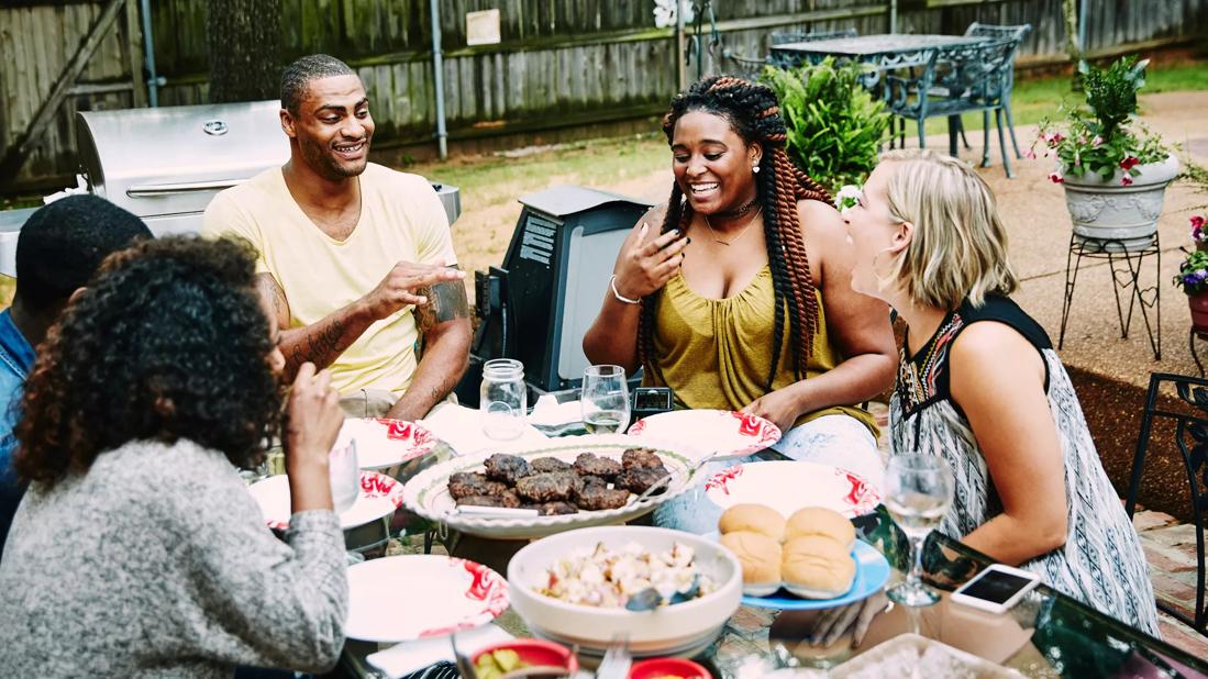 Group of happy people sitting around table full of food, having a cookout