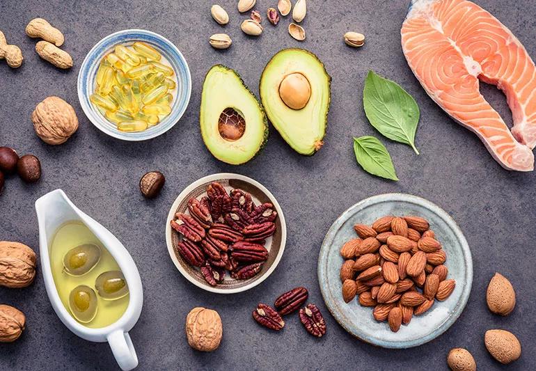 Counter filled with yellow supplements and healthy foods like salmon, nuts, olives and avocados