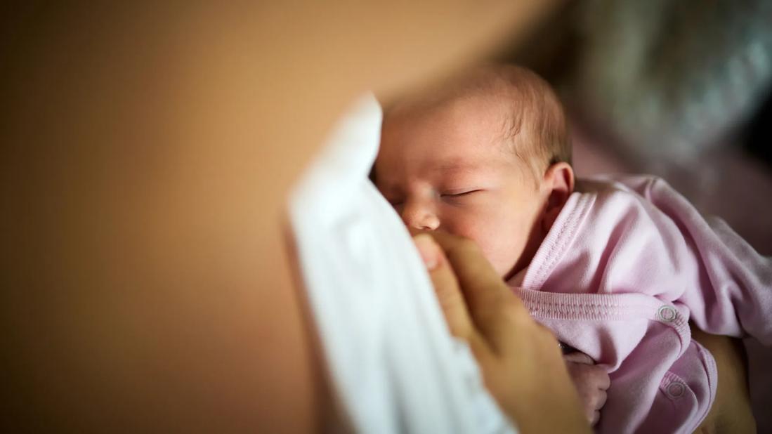 Newborn baby in pink shirt is nursing with caregiver