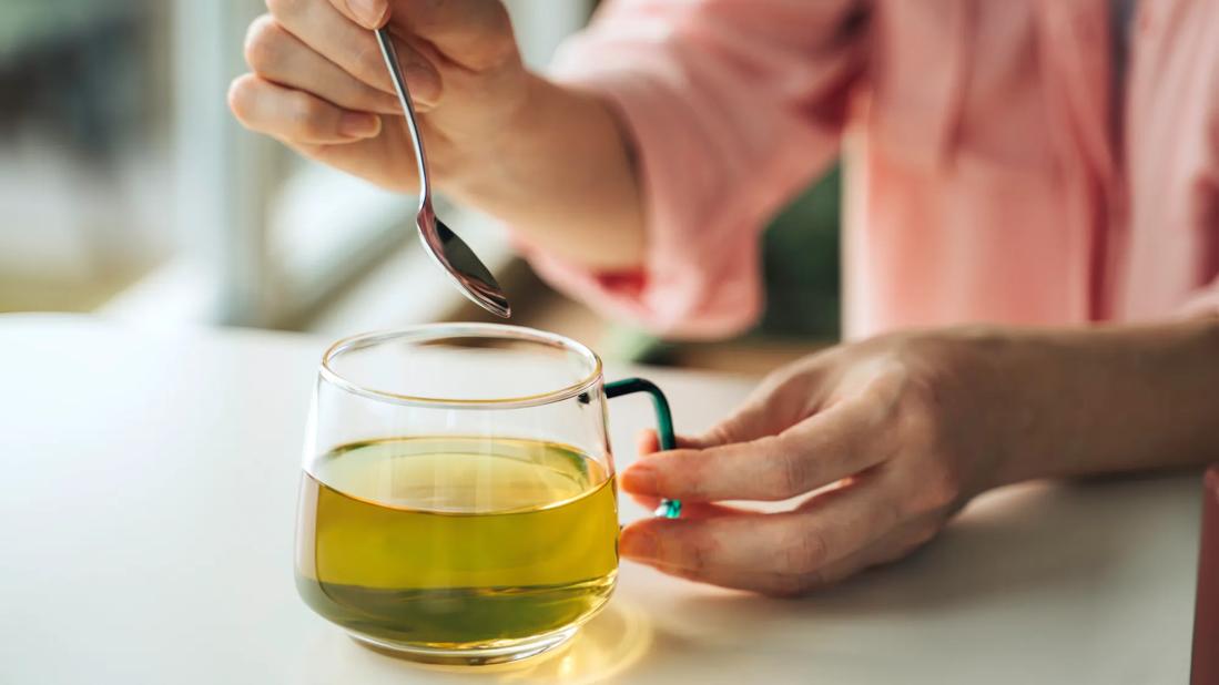 Person stirring glass mug of green tea with spoon