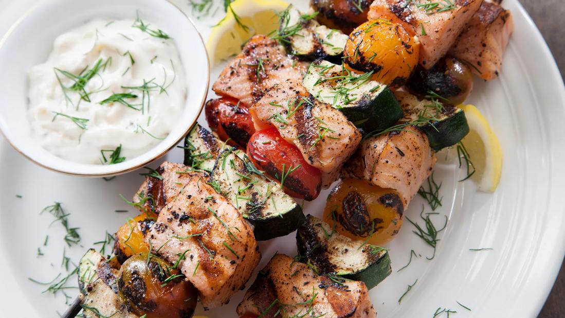 Grilled salmon chunks and veggies on skewers, with creamy dill yogurt sauce on the side