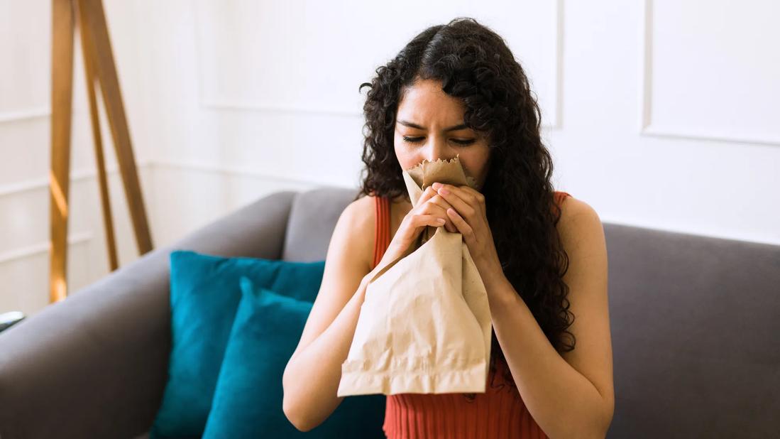 Person sitting on couch, breathing into a paper bag