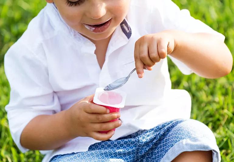 child sitting in grass eating yogurt