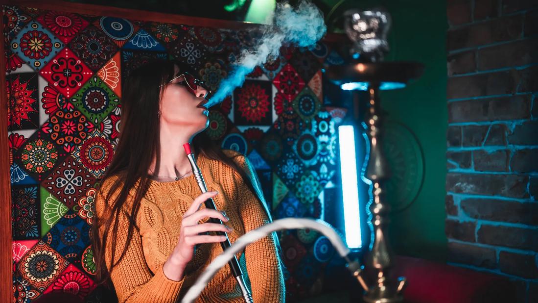 Person exhaling, with hookah wand in hand, in hookah den