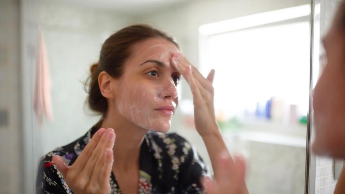 Person in bathroom looking in mirror washing face with fingers