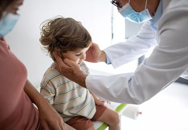 Young boy receives a hearing exam as doctor feels the backs of his ears while his mother looks on